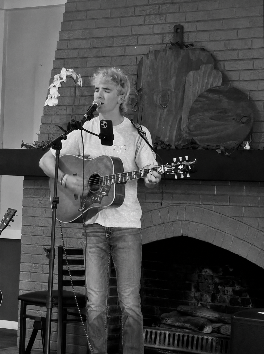 Ryan North performing acoustic guitar and singing in front of a brick fireplace